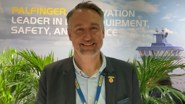 Portrait of a man, Gunther Fleck, standing in front of a booth wall and plants, smiling into the camera.