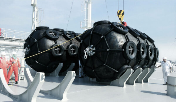 Two PALFINGER fenders on deck of a vessel during their installation conducted by three workers, one sitting on top of a fender, the others holding a rope for stability.