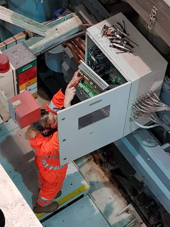 Woman in workwear, doing some works on what seems like a generator.