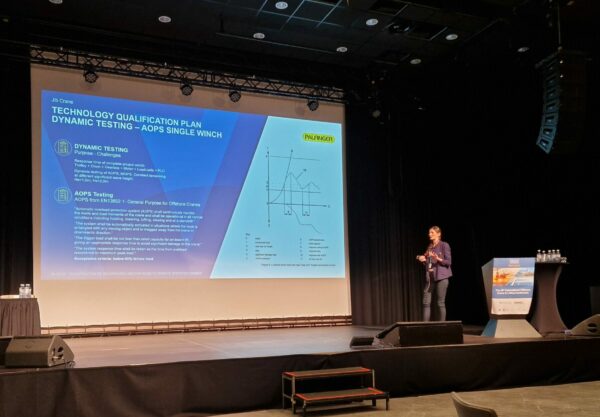 Woman standing on a stage, next to a beamer. She gives a presentation about PALFINGER MARINE's new offshore lifting innovation - the fully electric jib crane.