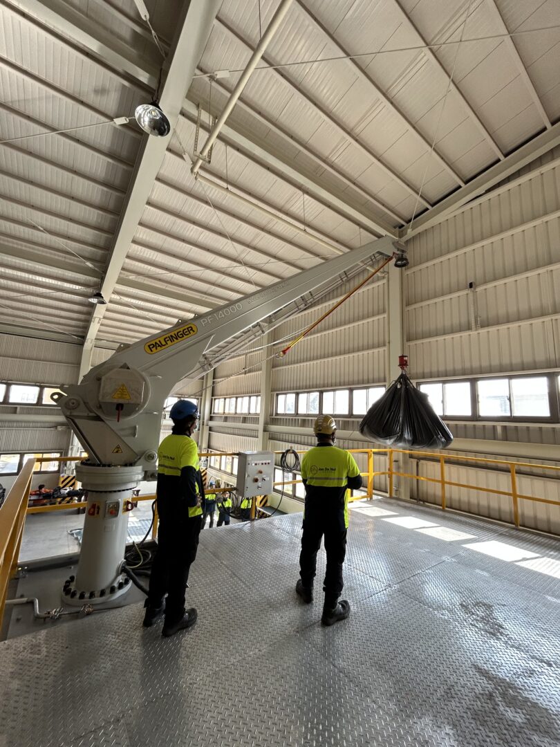 Two people next to a crane. One of them holding a controller, performing load tests with the crane.