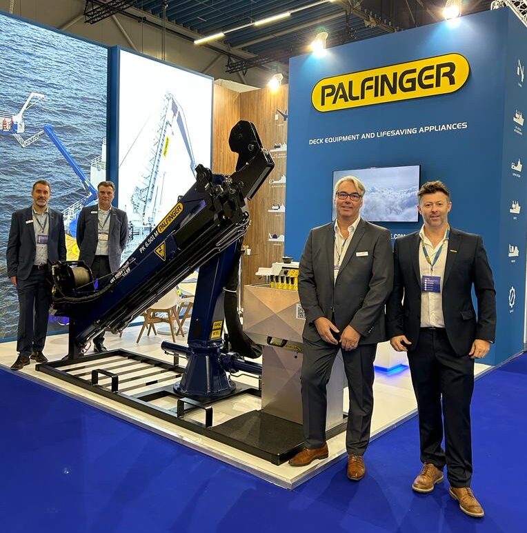 Four man standing at PALFINGER MARINE's exhibition stand at the Europort trade fair 2024 - two to the left side of a full-scale crane, two to the right of the crane.
