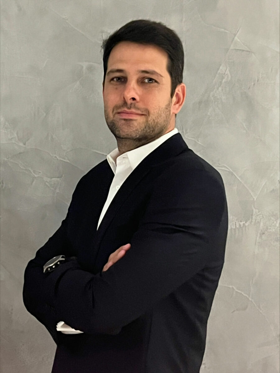 Portrait of Guilherme Felix on a grey background. He is wearing a suit jacket and a white shirt.
